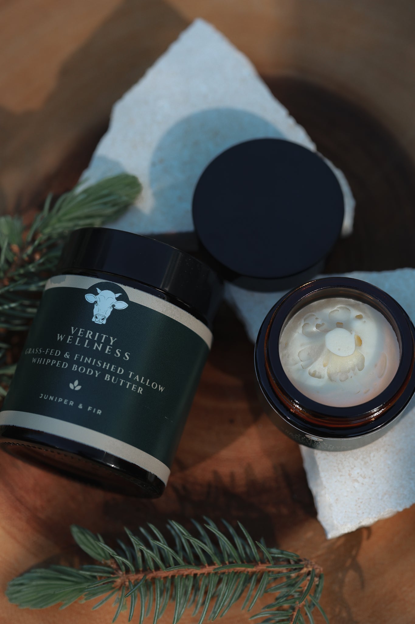 Organic tallow Body butter jar with open lid on a textured surface with greenery