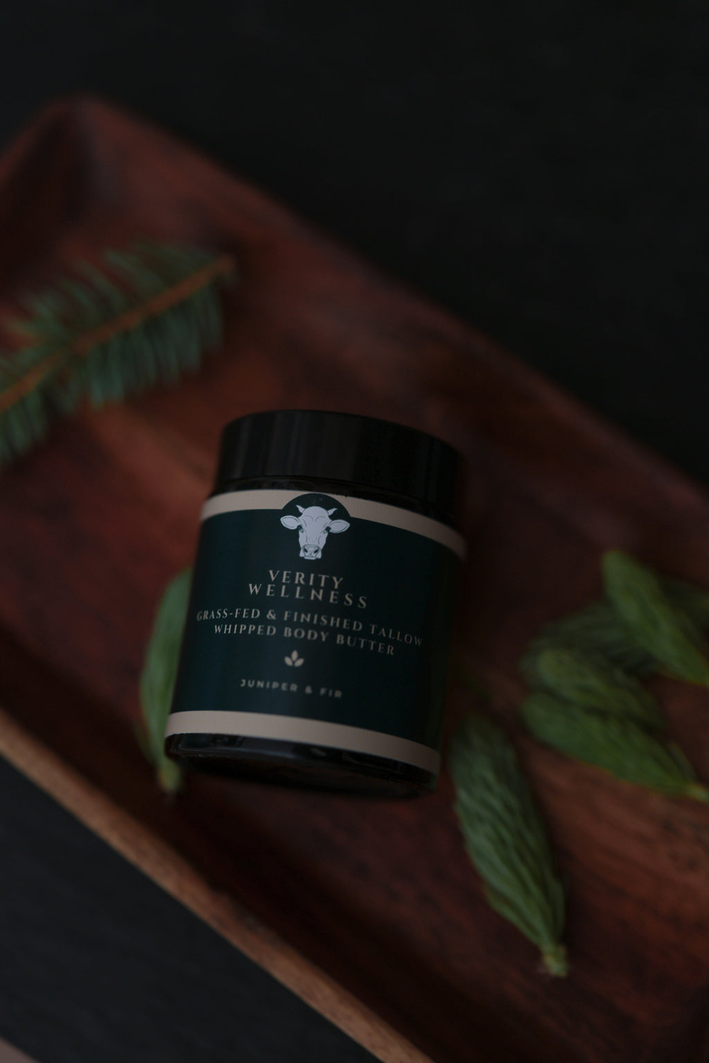 Jar of Verity Wellness whipped organic tallow body butter on a textured surface with green leaves.